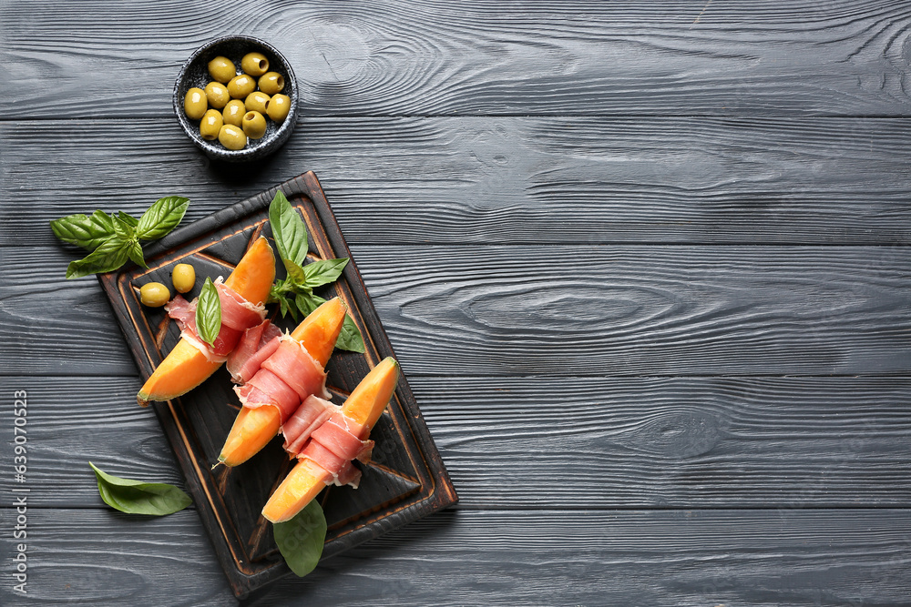 Tasty melon with prosciutto, basil and green olives on dark wooden background