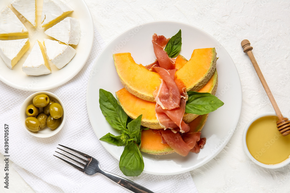 Composition with plate of tasty melon, prosciutto, cheese and olives on light background