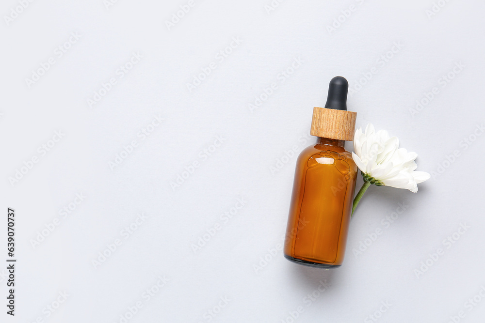 Bottle of essential oil with chamomile flower on light background