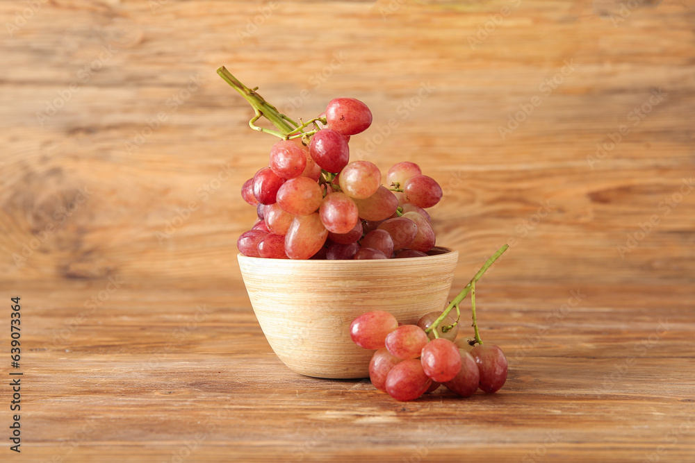 Bowl with tasty ripe grapes on wooden background