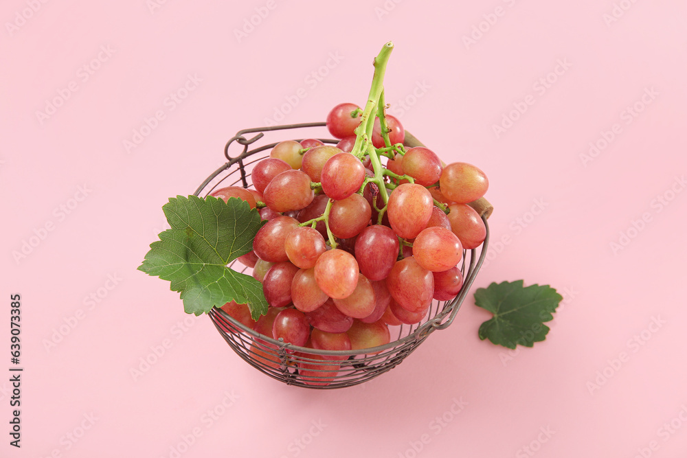 Basket with tasty ripe grapes on pink background