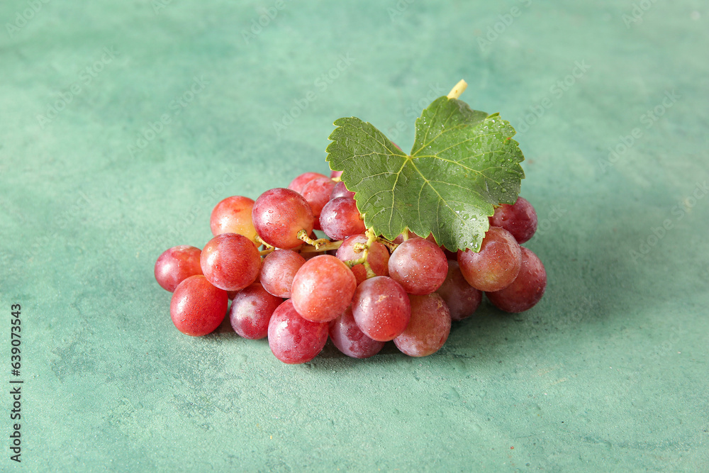 Tasty ripe grapes with leaf on green background