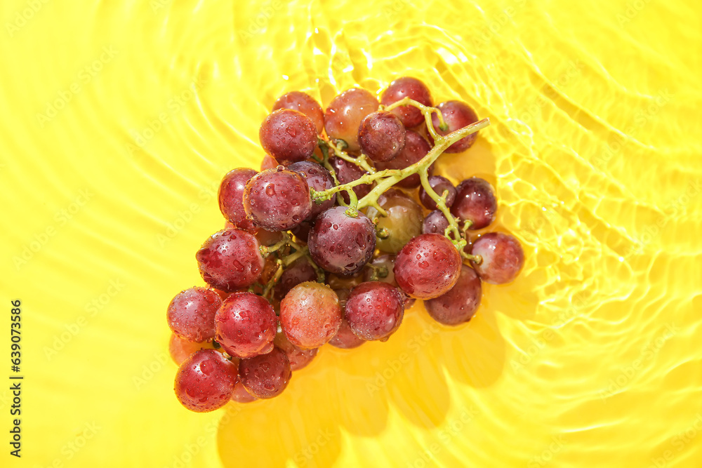 Tasty ripe grapes in water on yellow background