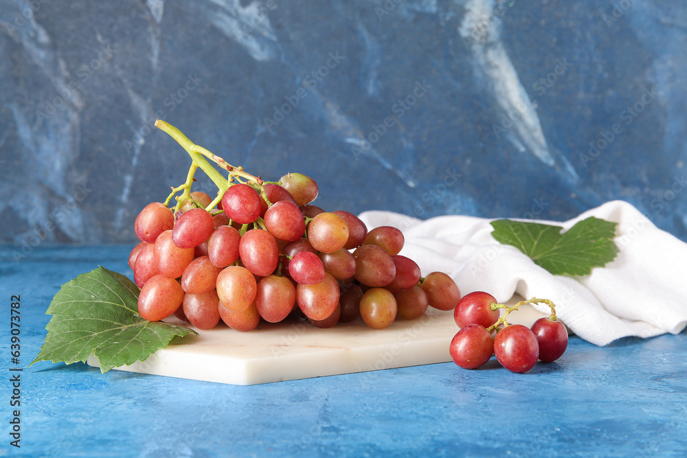 Board with tasty ripe grapes on blue background