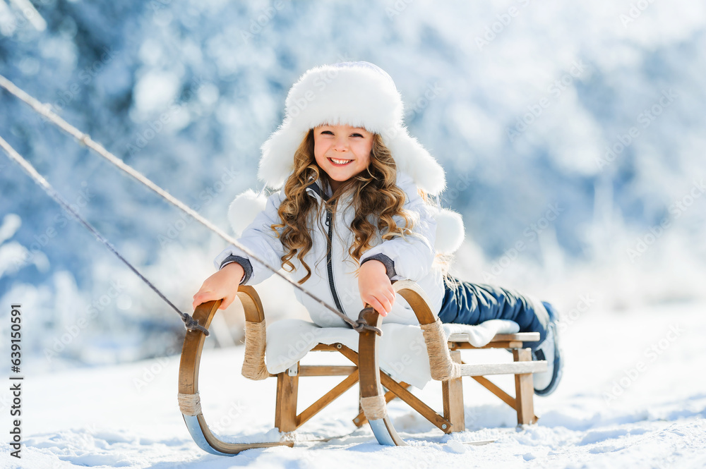 Happy cute kid having fun on sled in winter time. Warm winter clothes.