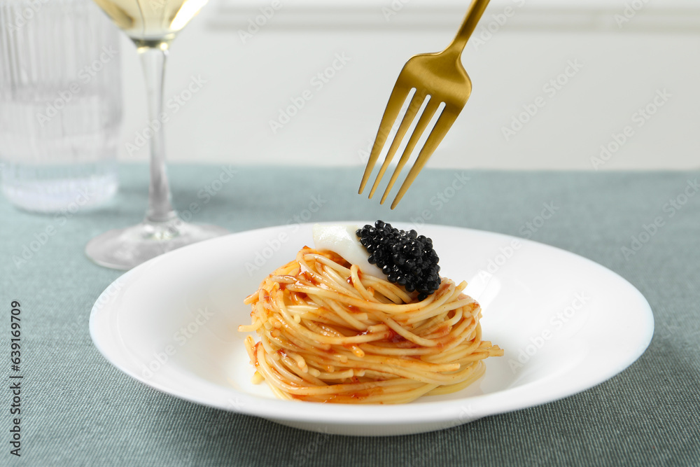 Eating tasty spaghetti with tomato sauce and black caviar at table, closeup. Exquisite presentation 