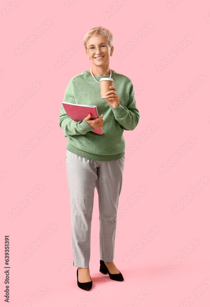 Beautiful mature woman with magazines and cup of coffee on pink background