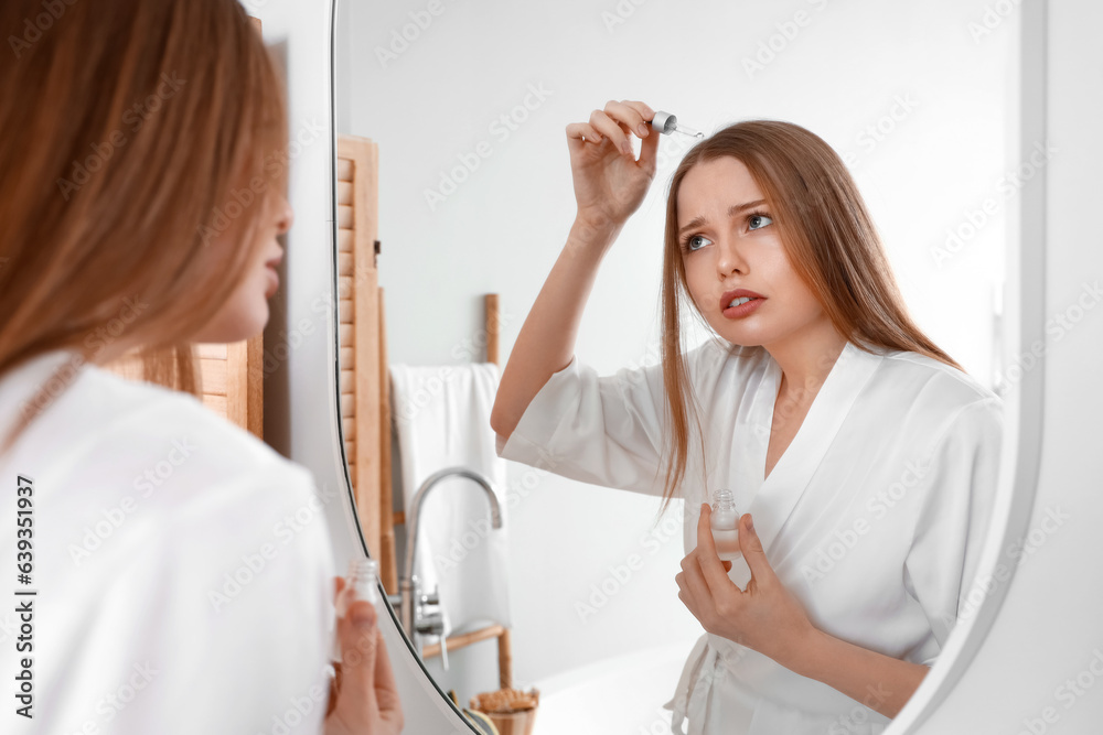 Young woman using serum for hair loss treatment at home