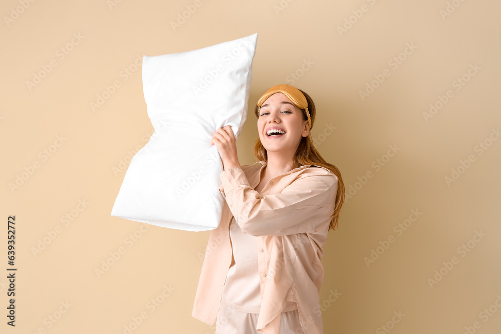 Young woman in pajamas with pillow on beige background