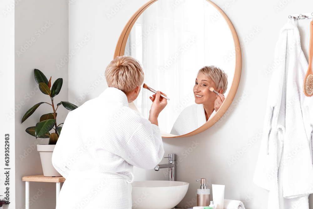 Mature woman doing makeup near mirror in bathroom