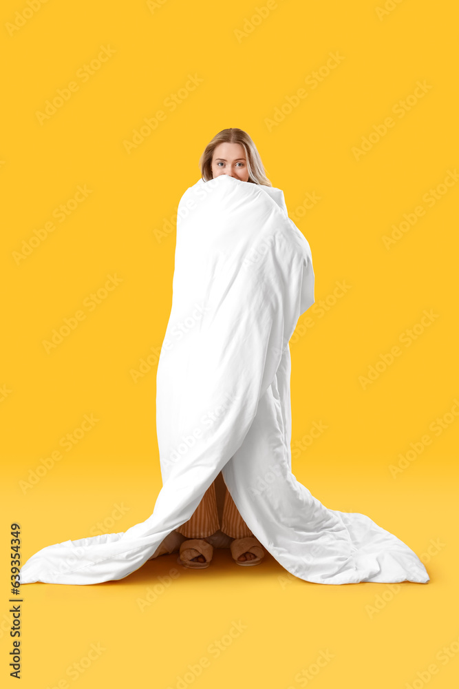 Young woman with blanket on yellow background