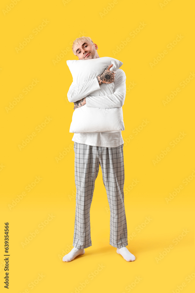 Young tattooed man with soft pillow on yellow background