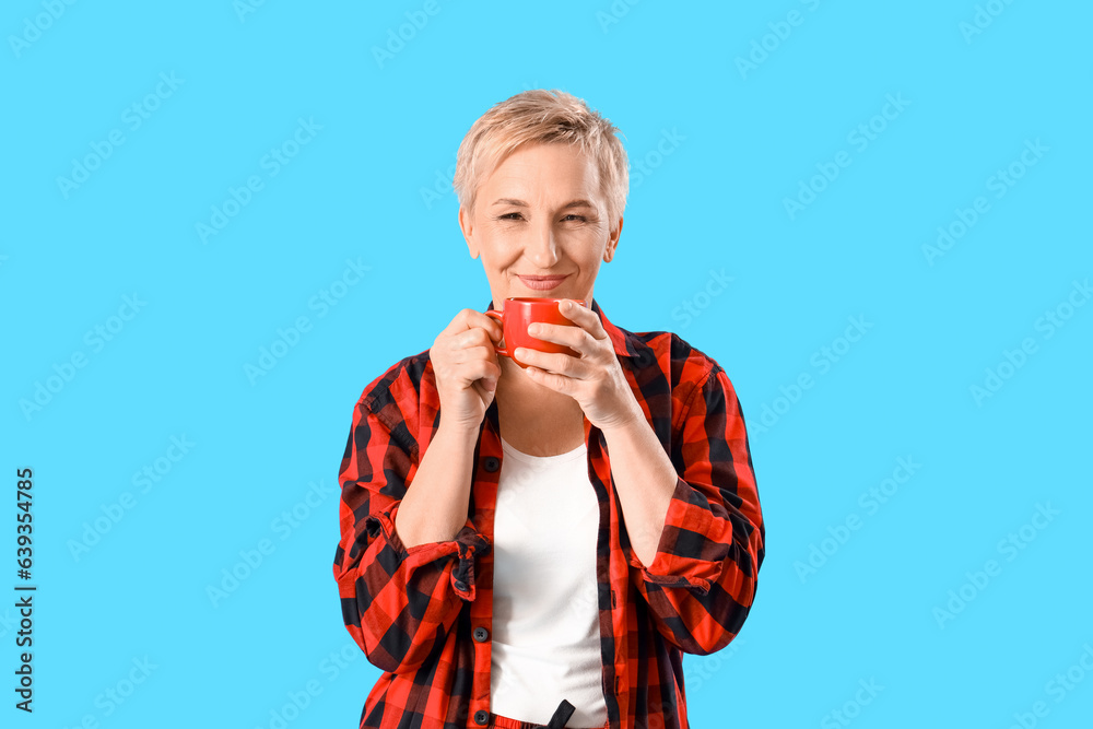 Mature woman in pajamas with cup of coffee on blue background