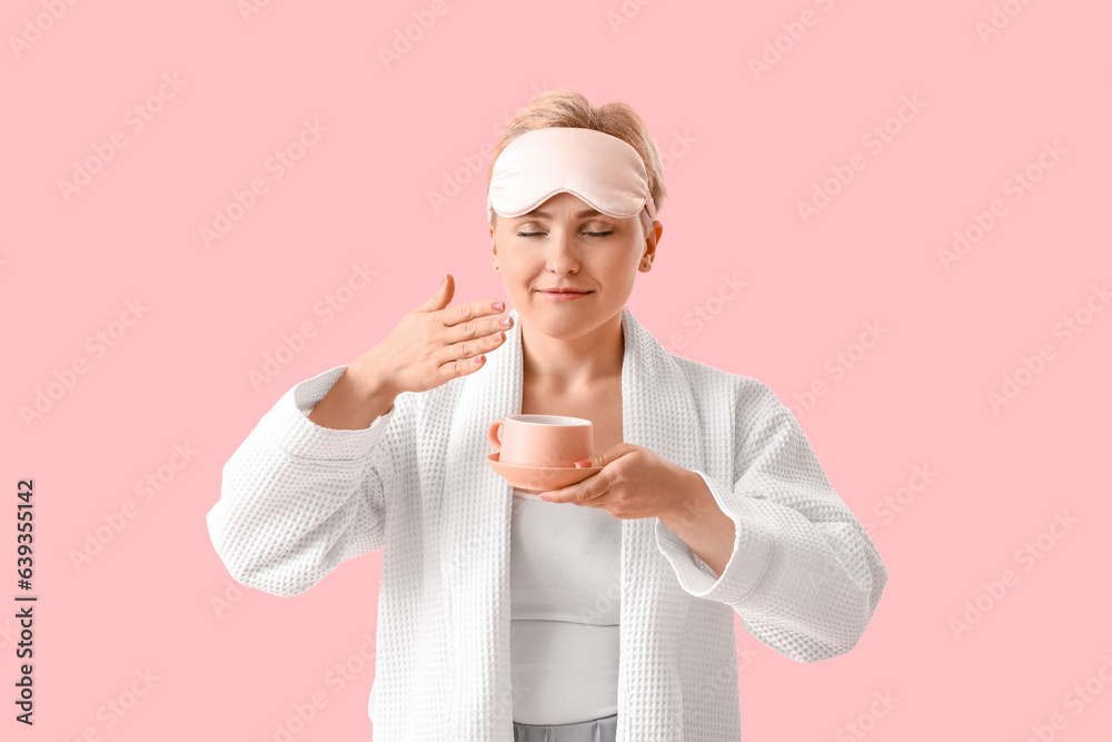 Young woman in sleeping mask with cup of coffee on pink background