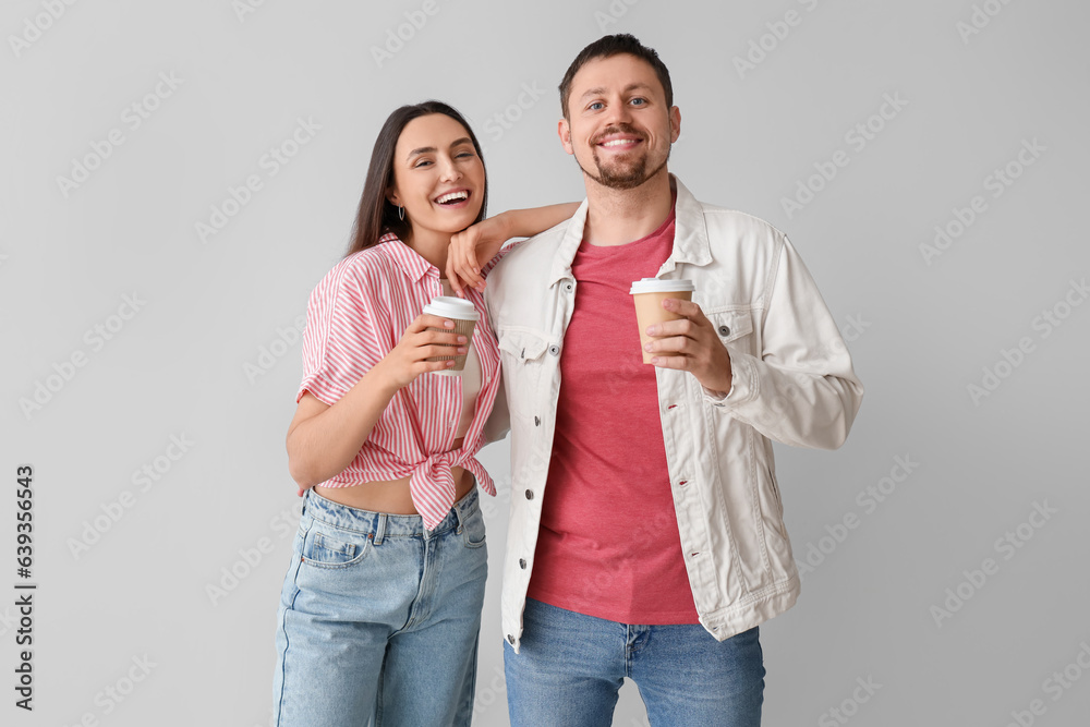 Happy young couple with cups of coffee on light background