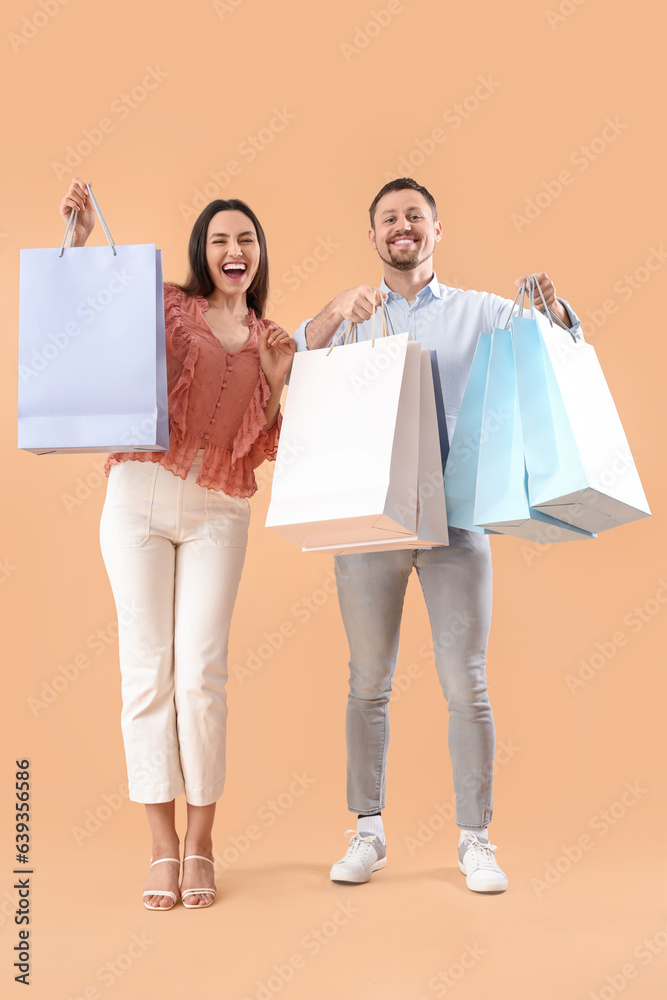 Happy young couple with shopping bags on beige background