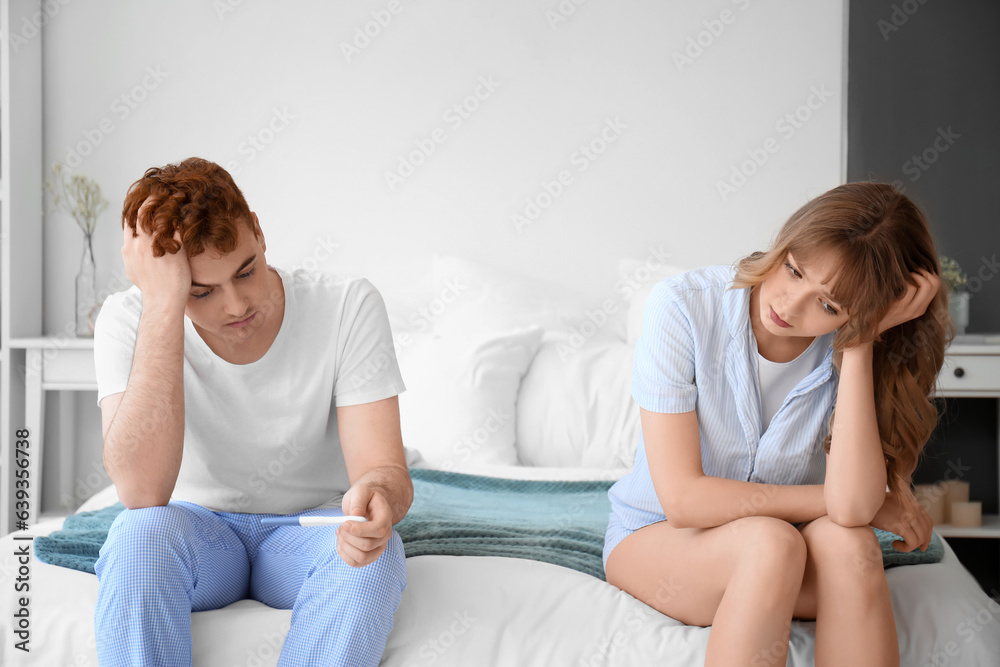 Sad young couple with pregnancy test in bedroom