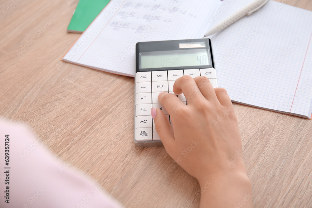 Woman working with calculator on wooden table, closeup