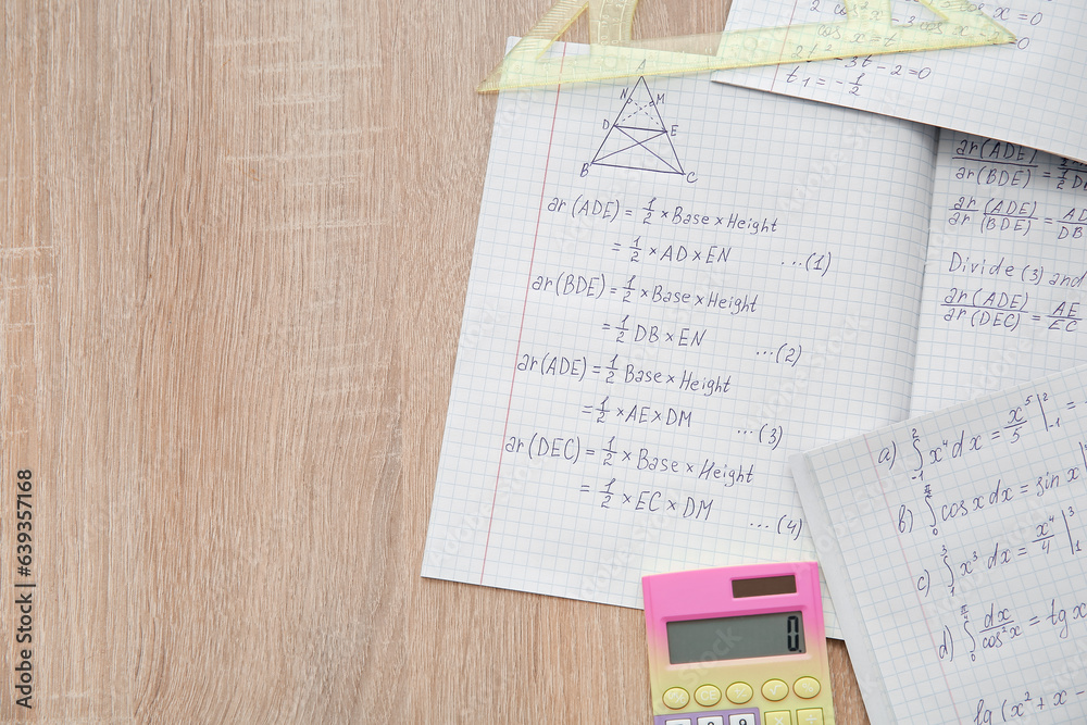 Open copybooks with math formulas and stationery on wooden table