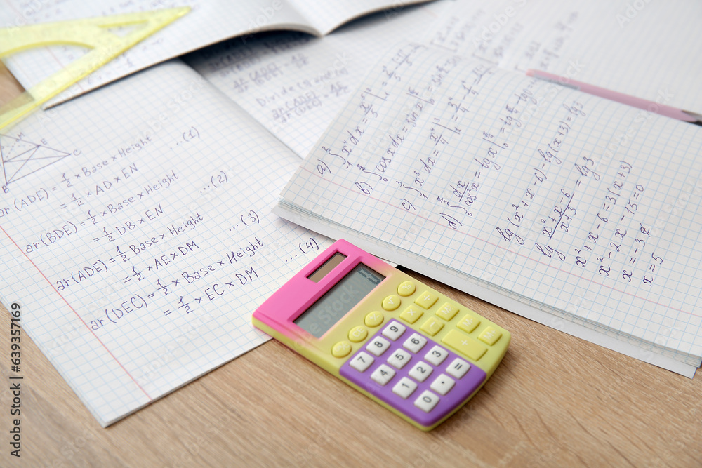 Open copybooks with math formulas and stationery on wooden table