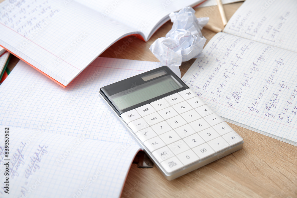 Calculator and copybooks with math formulas on wooden table