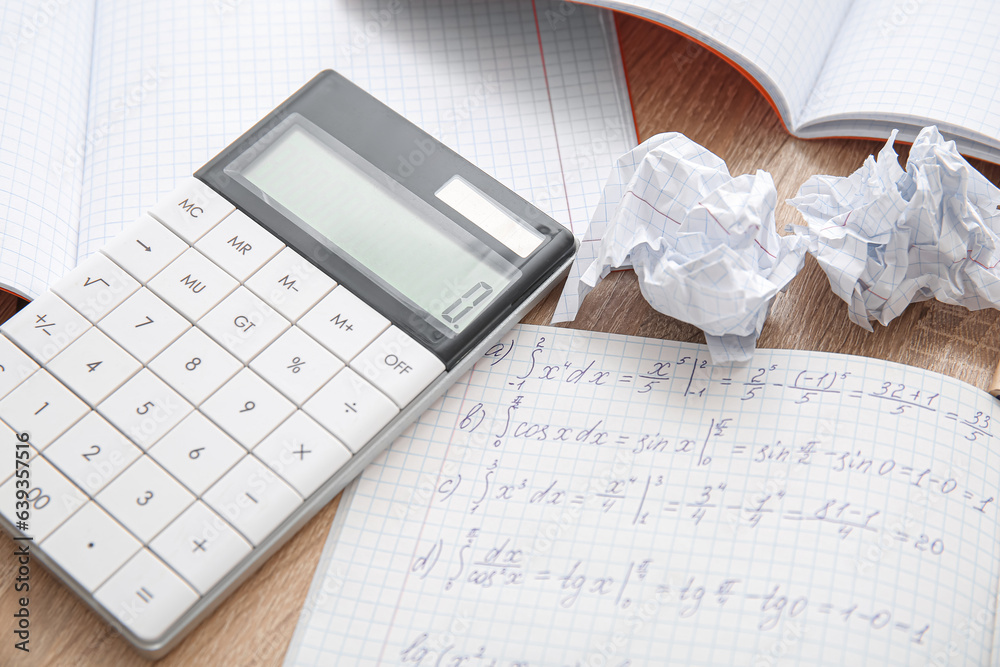 Calculator, copybook with math formulas and crumbled paper on wooden table