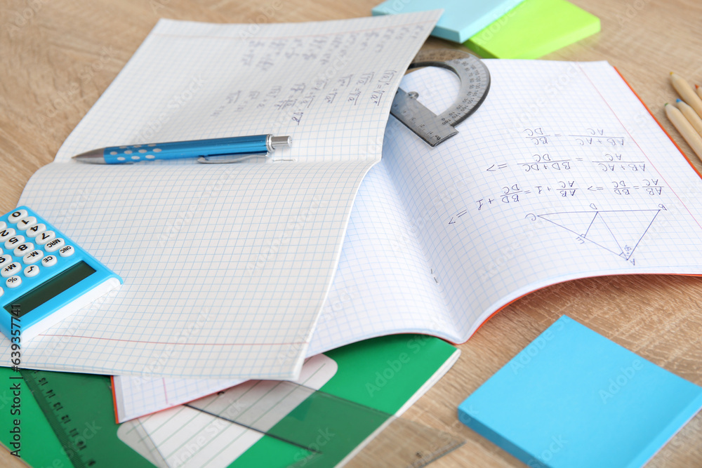 Open copybook with math formulas and stationery on wooden table, closeup