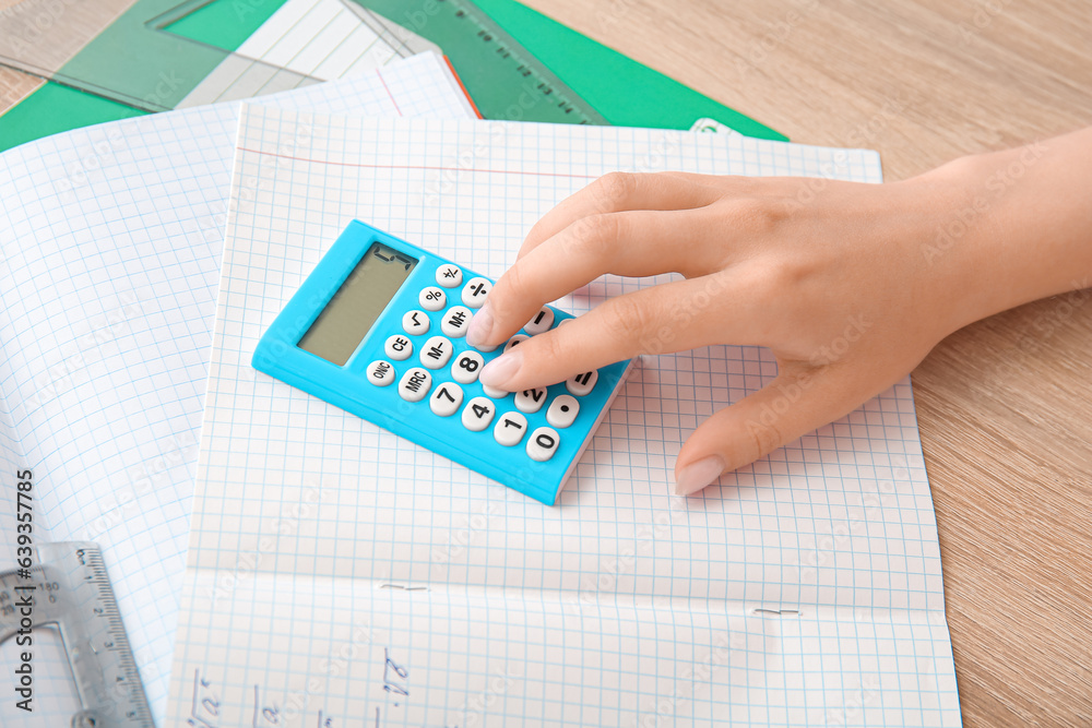 Woman working with calculator on wooden table, closeup