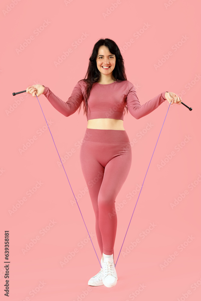 Sporty young woman with jumping rope on pink background