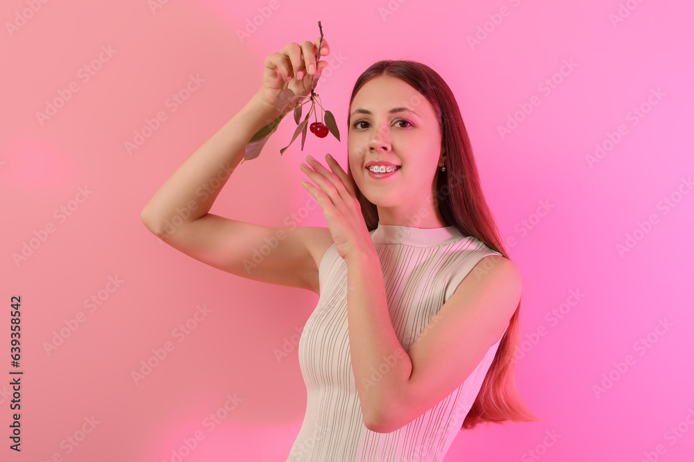 Beautiful young woman with branch of ripe cherries on pink background