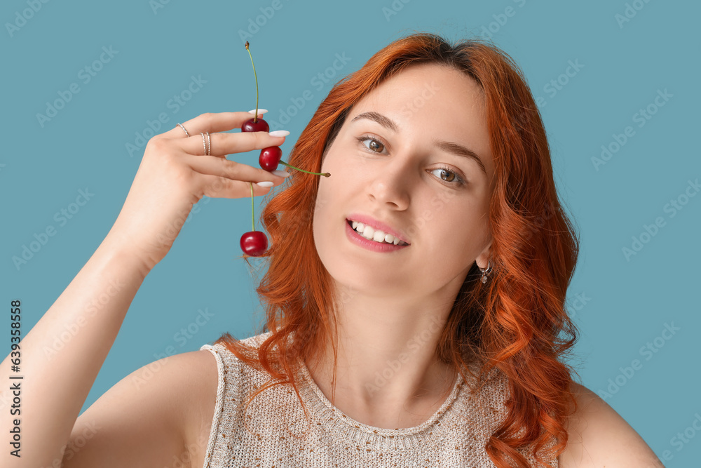 Happy beautiful young woman with many ripe cherries on blue background