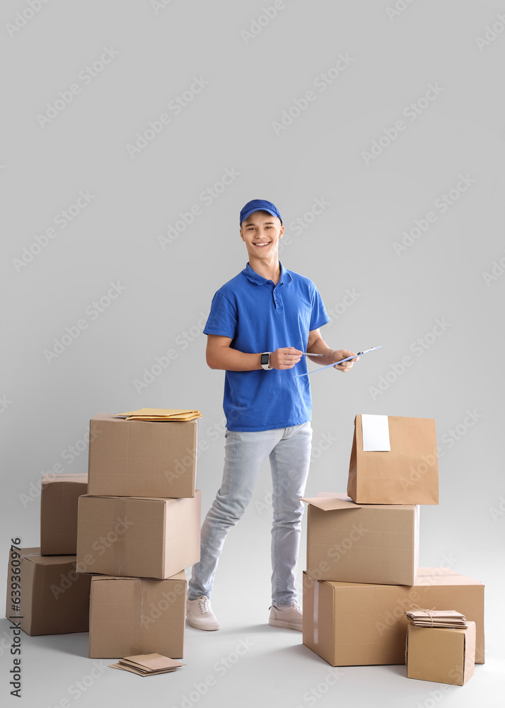 Young courier with clipboard and parcels on light background