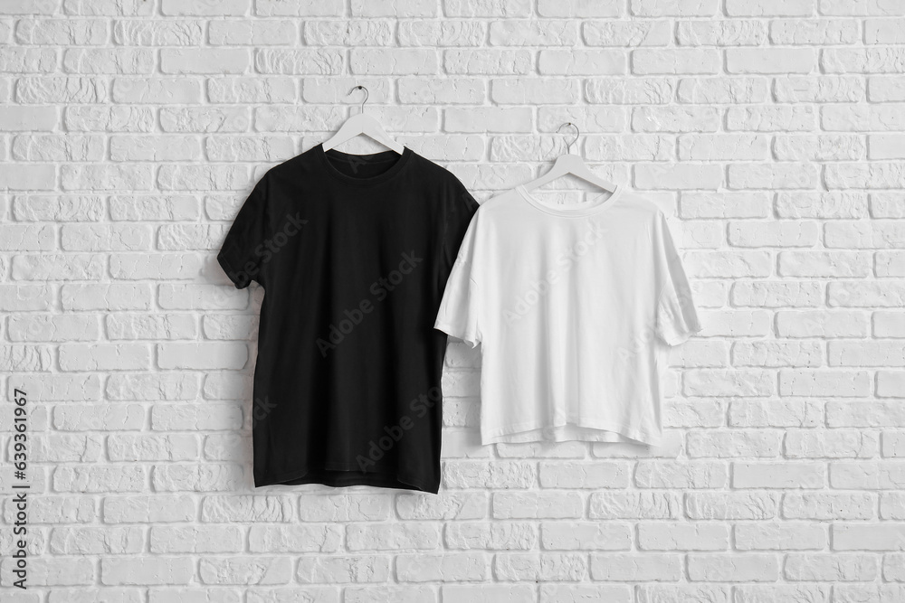 Stylish t-shirts hanging on white brick wall