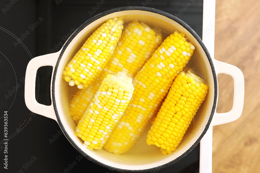 Cooking pot with boiling corn cobs on electric stove in kitchen