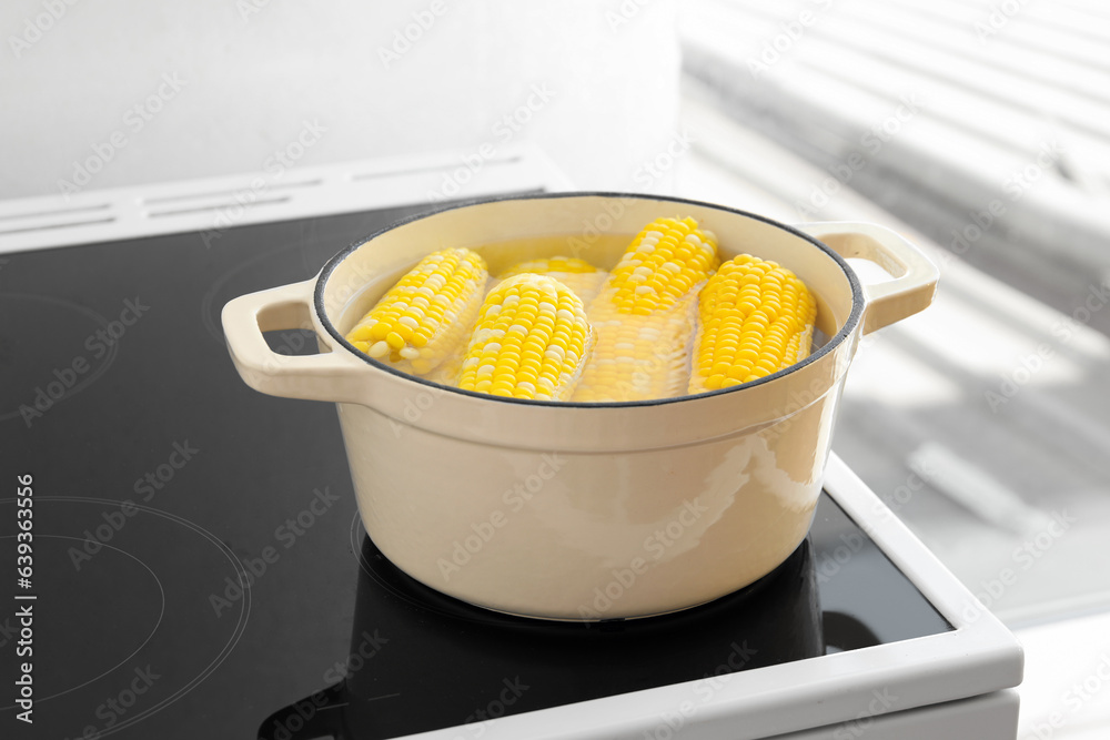 Cooking pot with boiling corn cobs on electric stove in kitchen