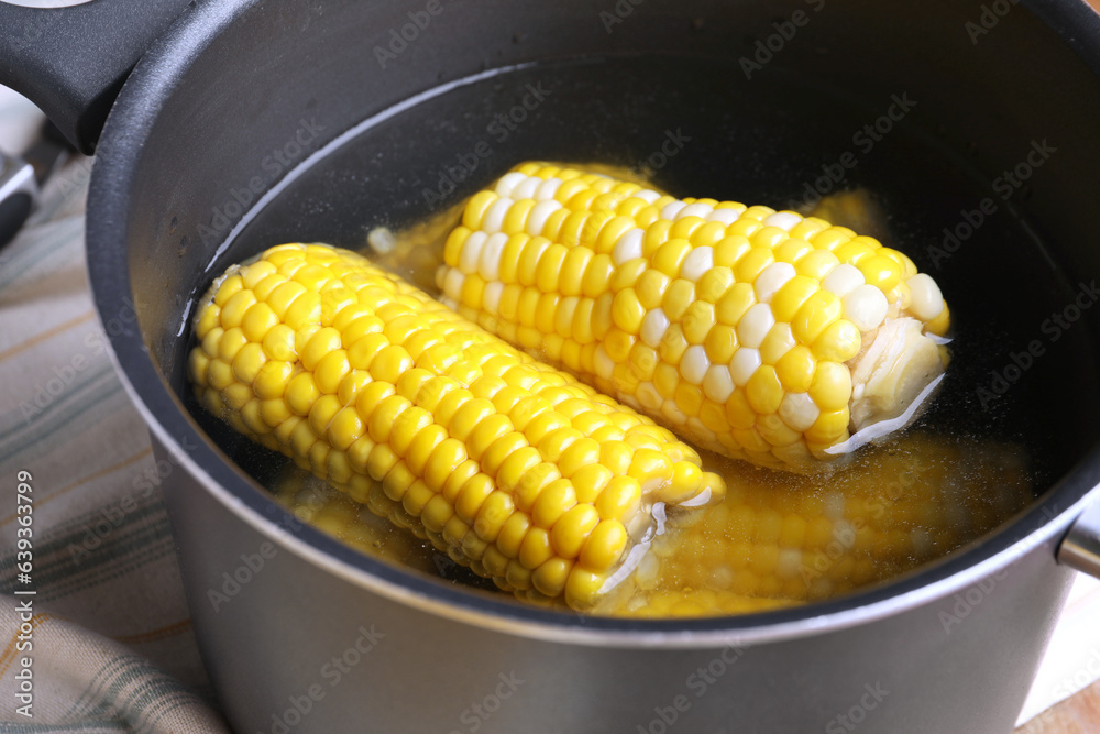 Cooking pot with boiled corn cobs on table, closeup