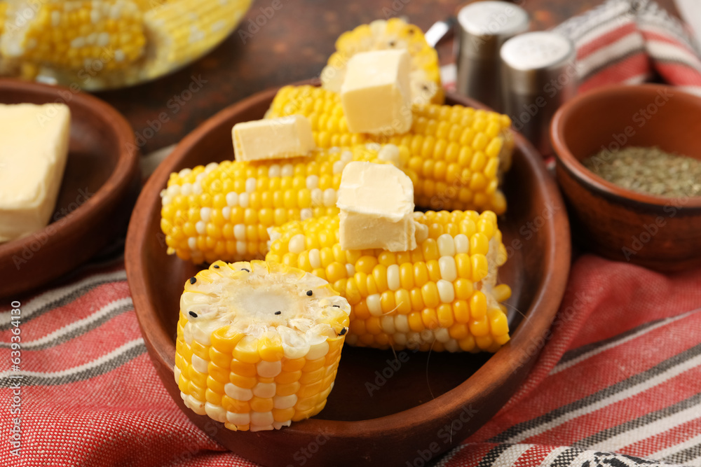 Plate of boiled corn cobs with butter on dark background