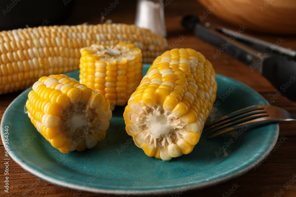 Plate with boiled corn cobs on wooden table