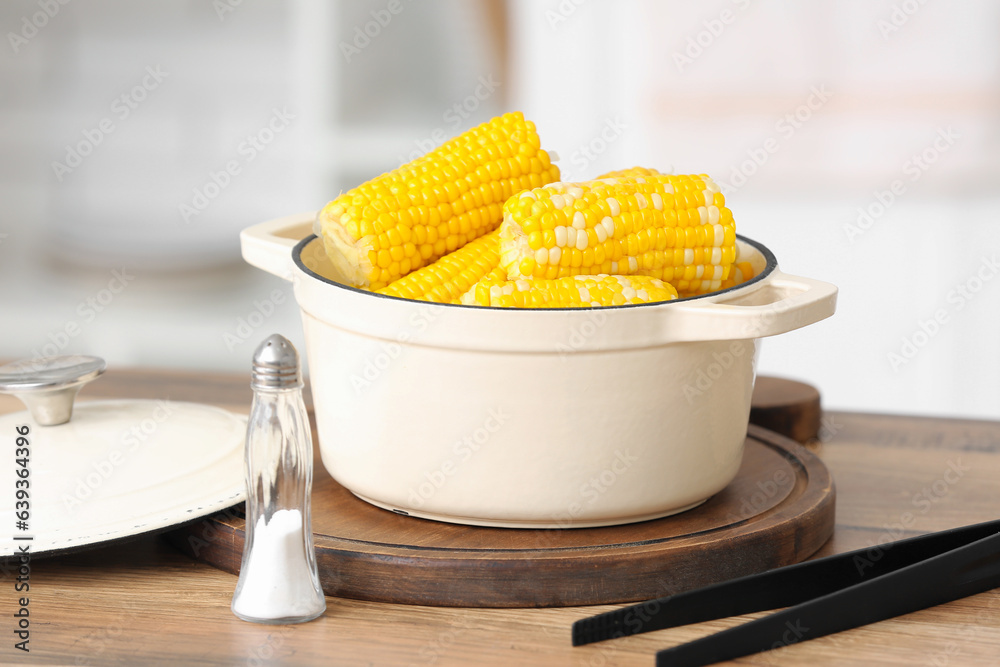 Cooking pot with boiled corn cobs on wooden table in kitchen