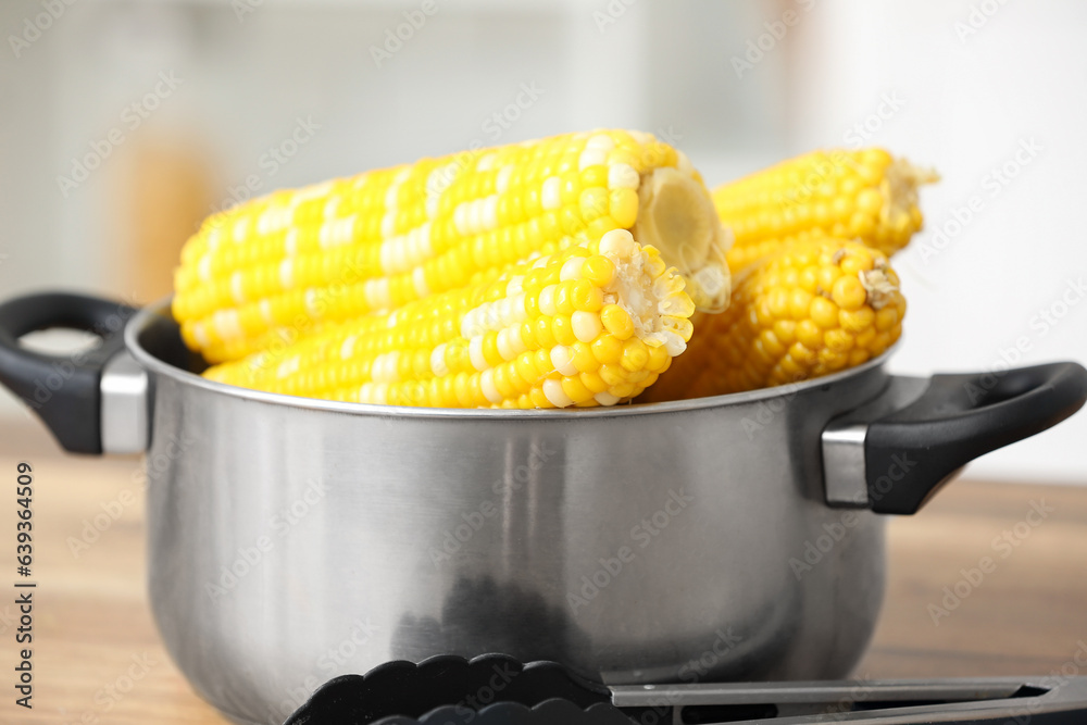 Cooking pot with boiled corn cobs on wooden table in kitchen