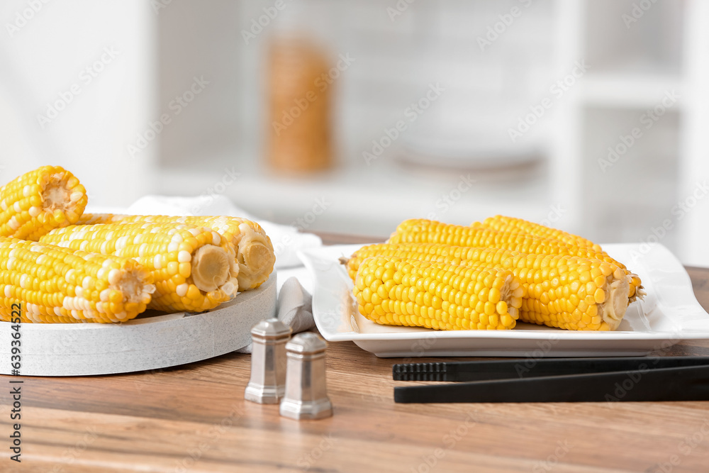 Plate and board with boiled corn cobs on wooden table in kitchen