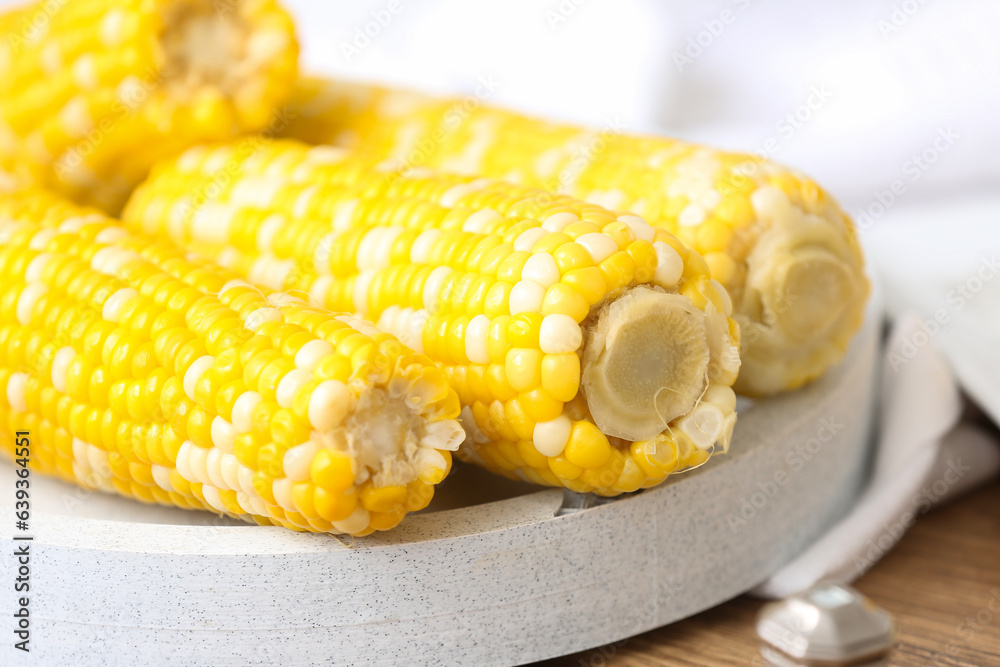 Board with boiled corn cobs on wooden table, closeup