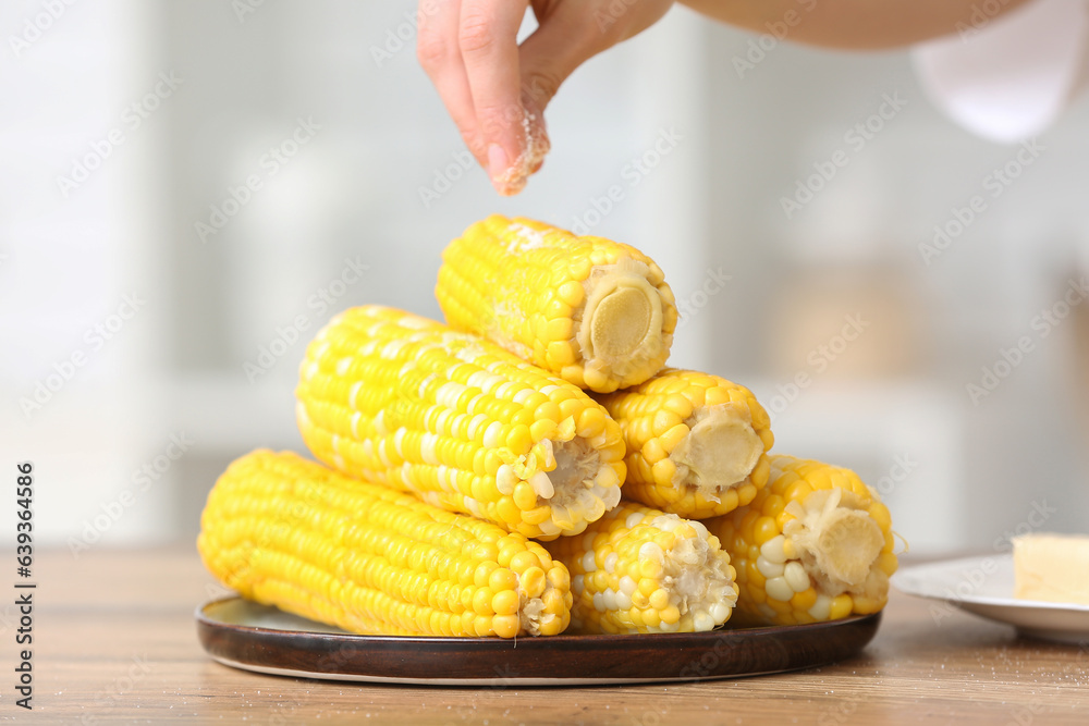 Woman salting boiled corn cobs on wooden table in kitchen