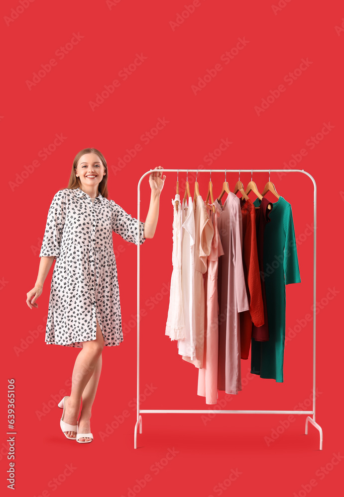 Pretty young woman near rack with dresses on red background