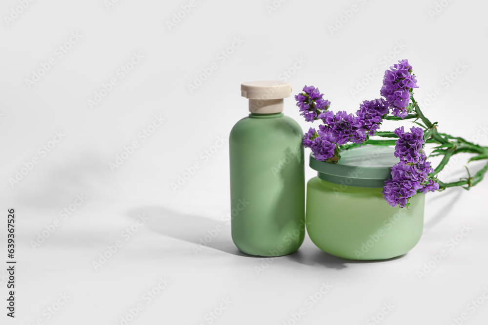 Bottle and jar of cosmetic products with beautiful flowers on white background