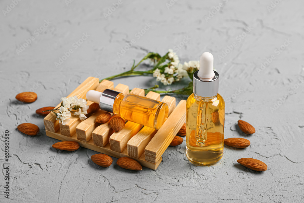 Bottles of cosmetic oil with beautiful flowers and almond on blue background