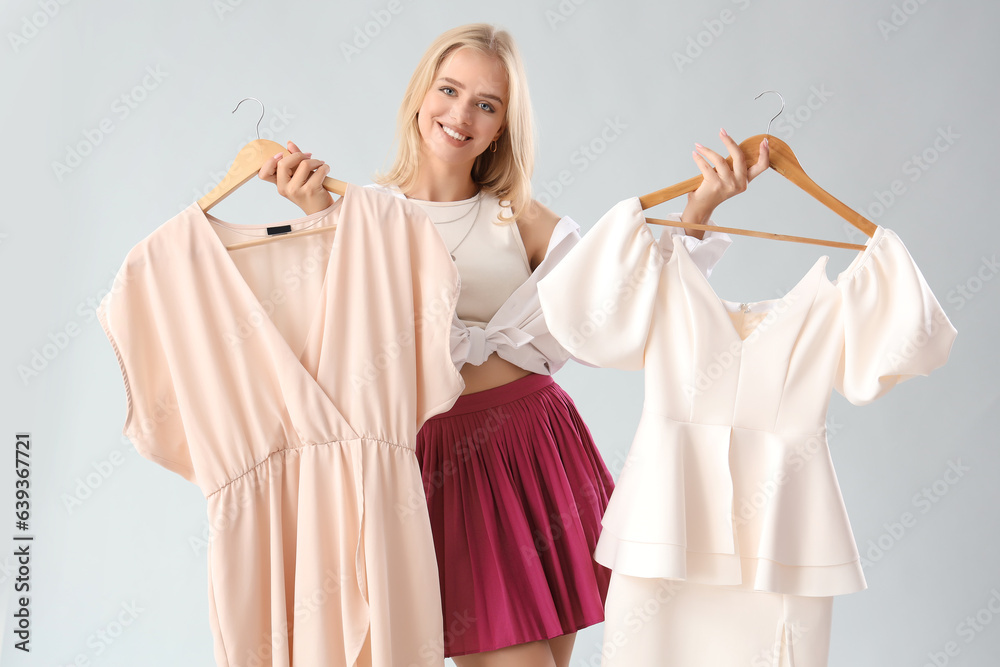 Beautiful young woman with new dresses on grey background