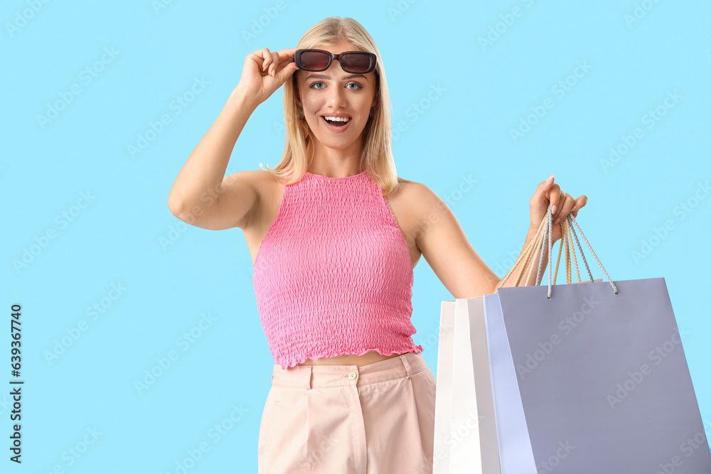 Beautiful young woman in sunglasses with shopping bags on blue background