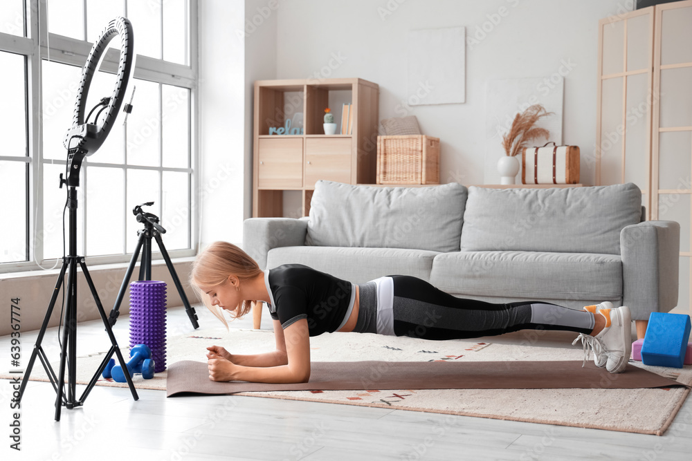 Beautiful young sport blogger recording video while training at home