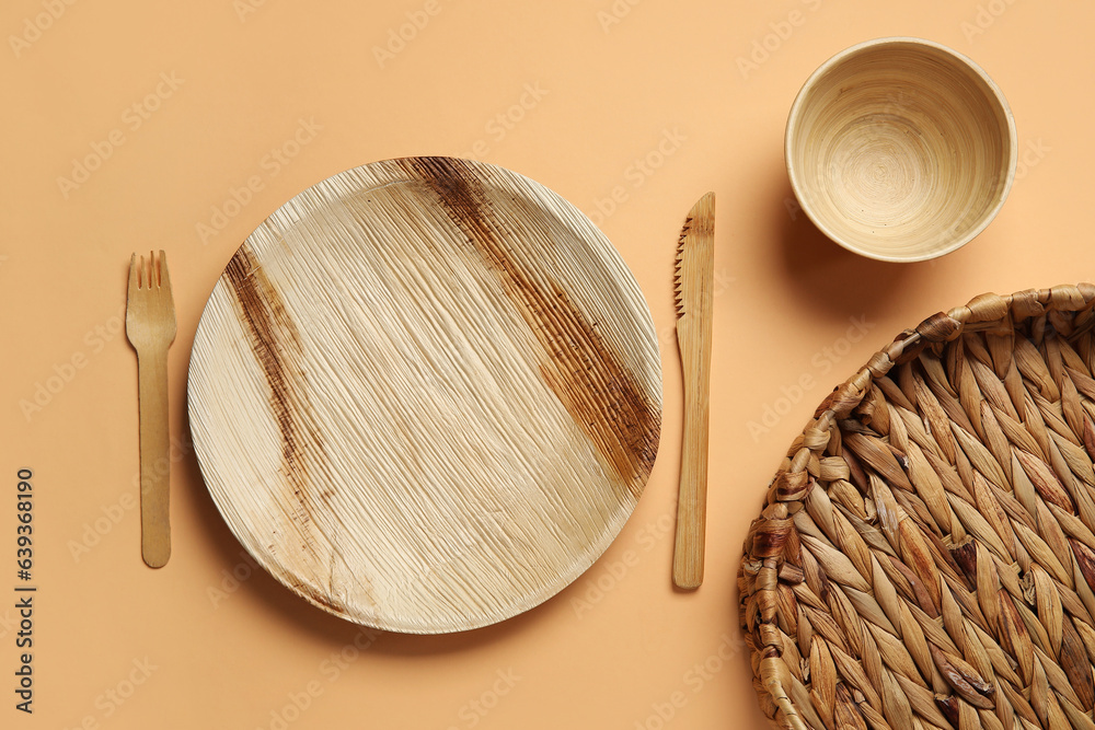 Wooden plate, bowl, cutlery and wicker tray on beige background